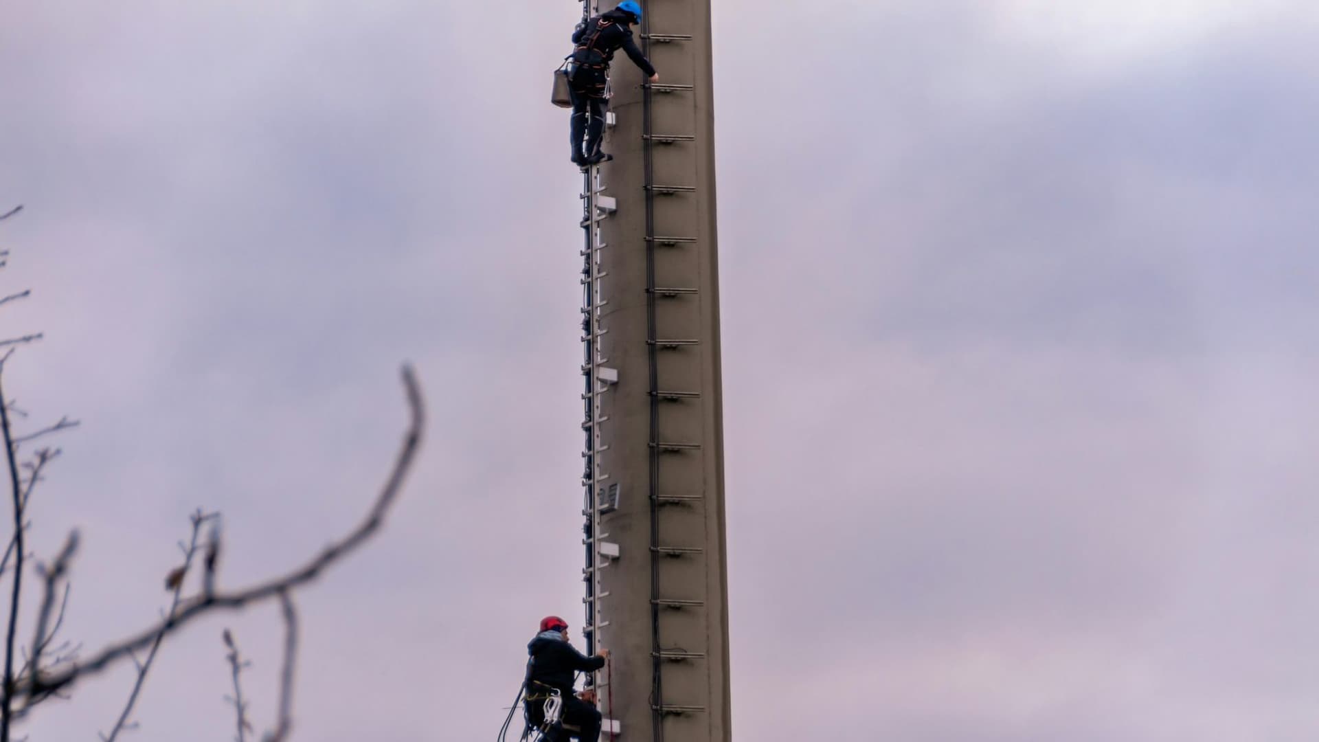 Telecom tower climbers wearing helmets and fall-arrest harnesses working at height.